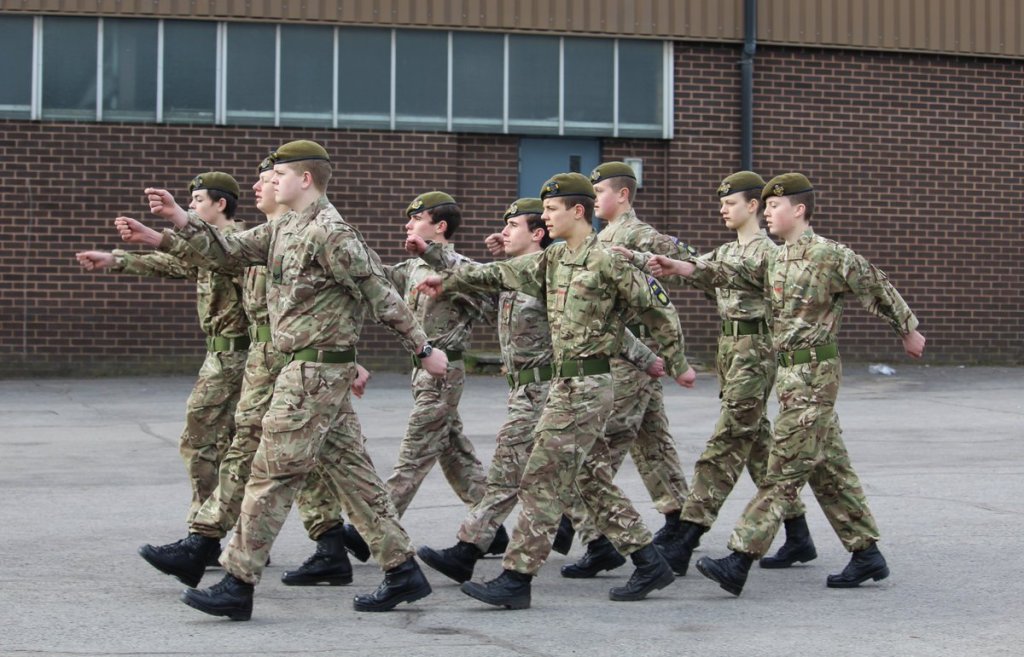 Image shows a group of nione youths in army uniform marchin in step.